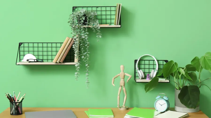 A wooden desk with accessories in a mesh holder, notebooks, small potted plant, desk clock, and a wooden sculpture.