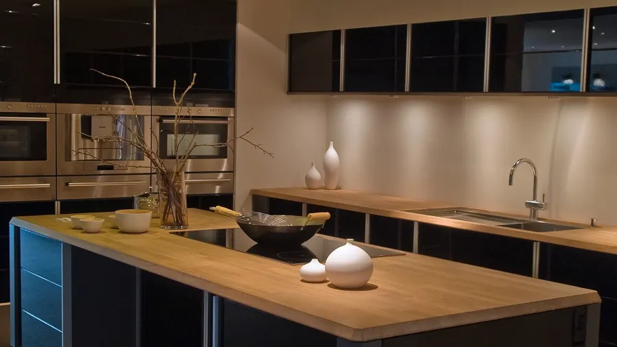 A modern kitchen interior with black cabinetry, wooden island and countertop, and stainless steel sink.
