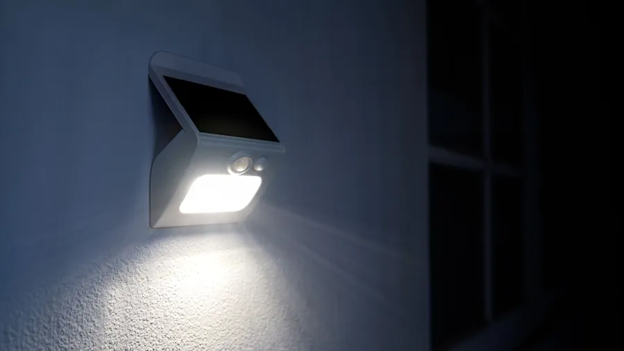 A solar powered motion sensor LED light on a white wall.