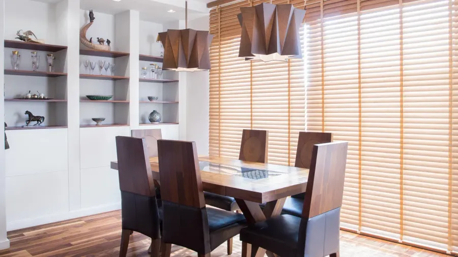 A dining room interior with oak wood table and chairs, built-in shelves with glassware and decor, and statement ceiling lights.