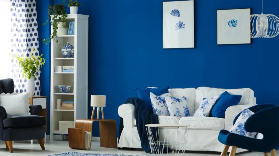 A living room interior with blue walls, wall art, coffee table, white shelf with decor accents, and armchairs.