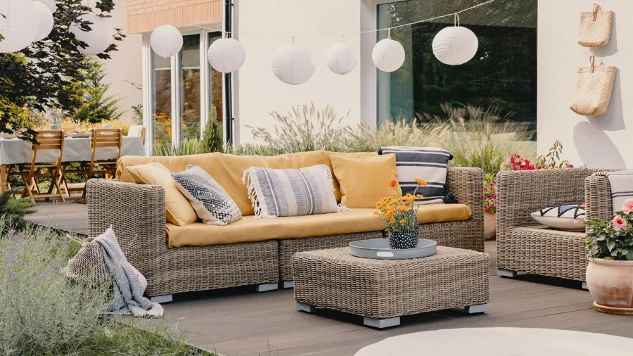 An outdoor seating area with a yellow couch and pillows, surrounded by plants and decorative lights.