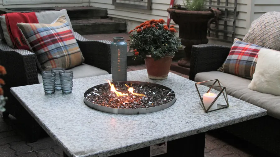 An patio with a firepit table, flower pot, sofas, throw pillows, and a candle.