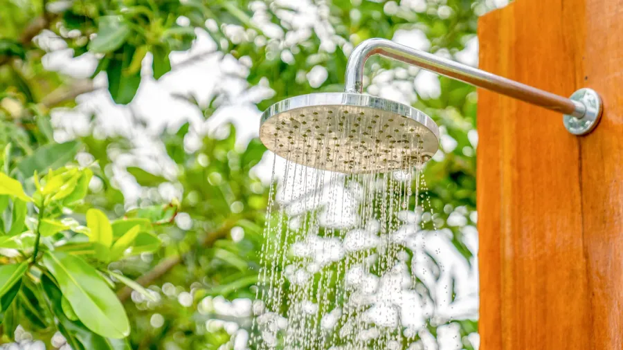 Outdoor shower with water spraying, set among green foliage.