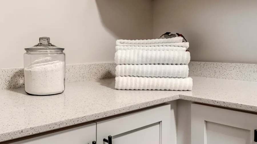 A laundry room with a detergent in a glass jar and folded towels placed on a quartz countertop.