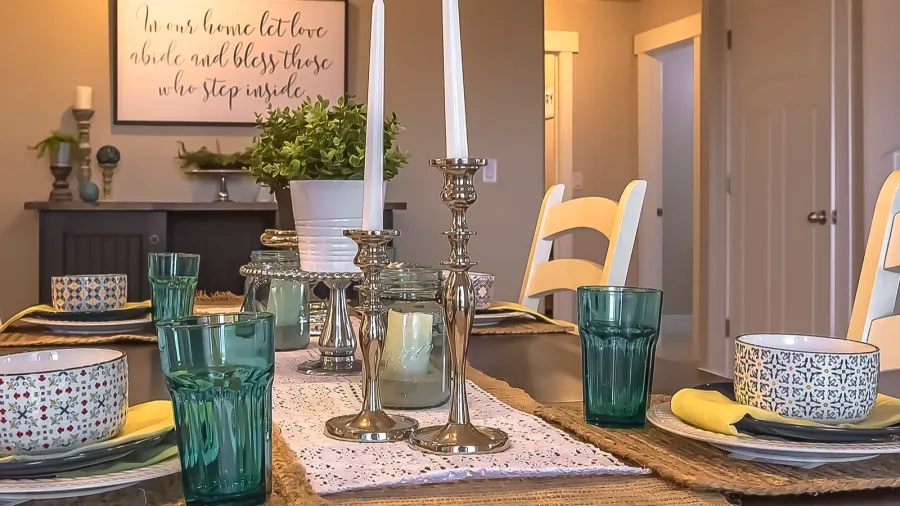 A beautiful table setting with candles in metallic holders, colorful glassware, and patterned dinnerware.
