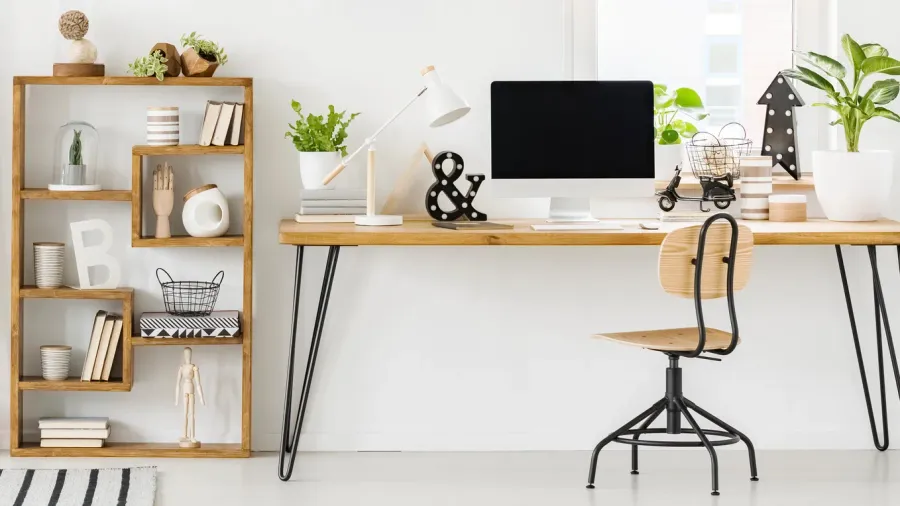 A home office interior with wooden desk, chair, and wooden bookcase with books and sculptural decor accents.