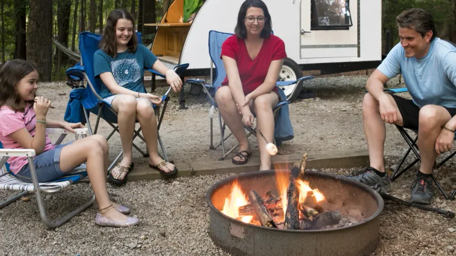 parents with children roasting marshmallows on campfire with teardrop camper