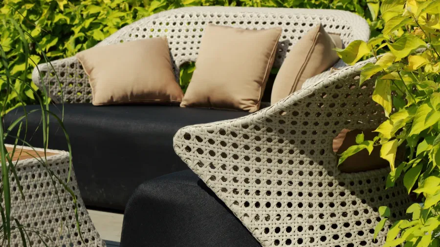 A stylish outdoor seating area with beige cushions and a dark table surrounded by green foliage.