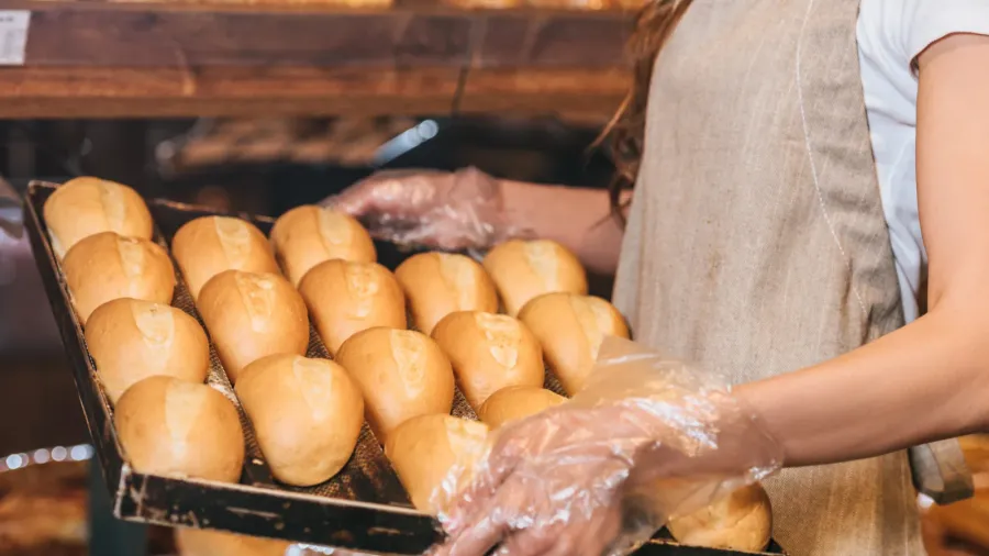 partial view of shop assistant arranging loafs of bread in