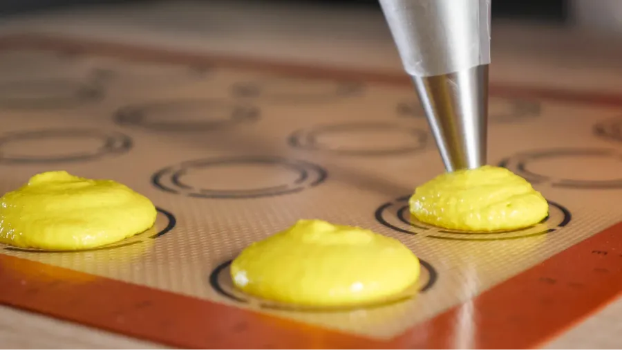pastry chef is cooking macaroons pouring dough on stencil silicone