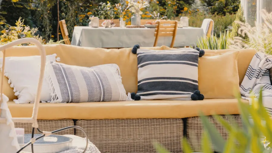 patterned pillows on a wicker couch in a garden blurred