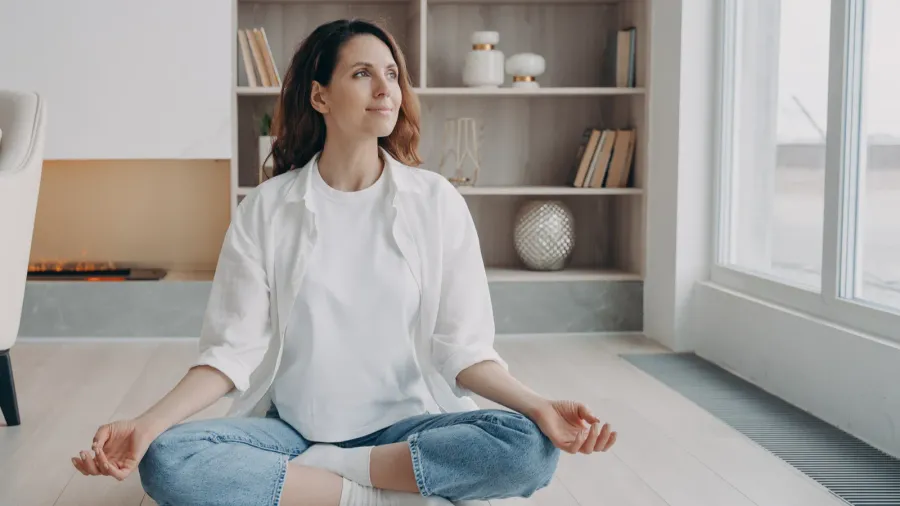 A cheerful woman practicing yoga while sitting in her living room.
