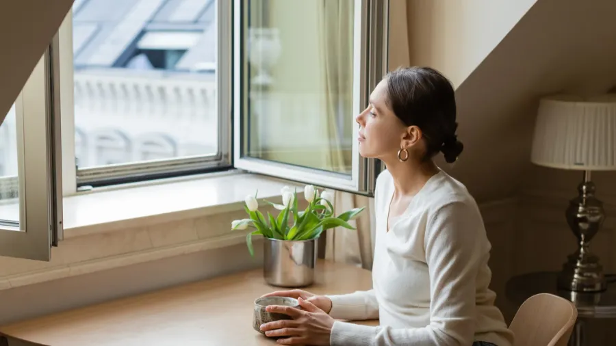 A woman relaxing by a window with a potted plant nearby.
