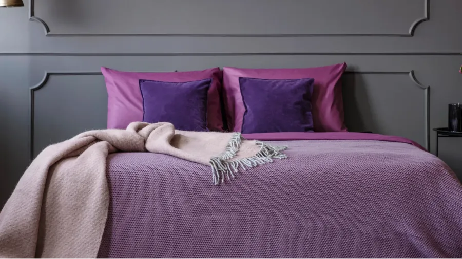 A chic bed adorned in shades of purple with a cozy throw, set against a textured gray wall for a sophisticated look.