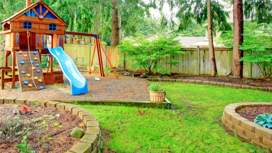 A colorful playground with a wooden treehouse, slide, and swing set amid green trees.