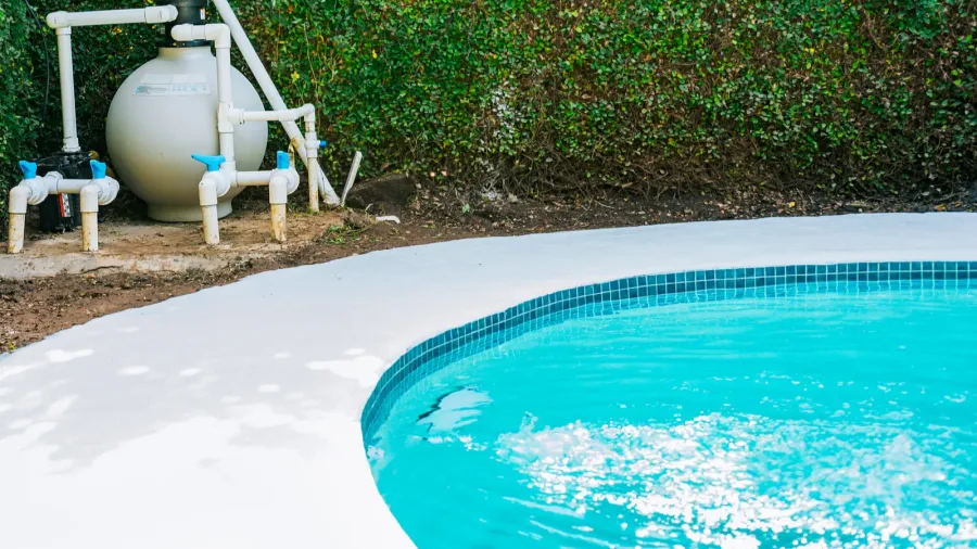Outdoor pool with a clean, white concrete surround and greenery.