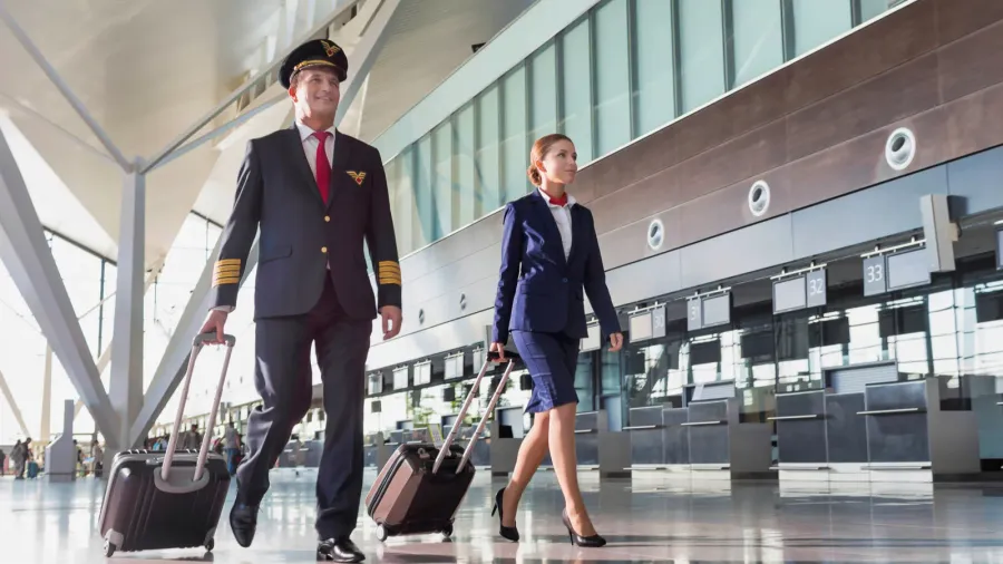 portrait of confident pilot with stewardess walking in airport