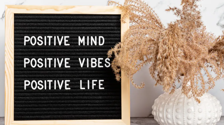 A framed quote and dried leaves in a vase on a wooden surface.