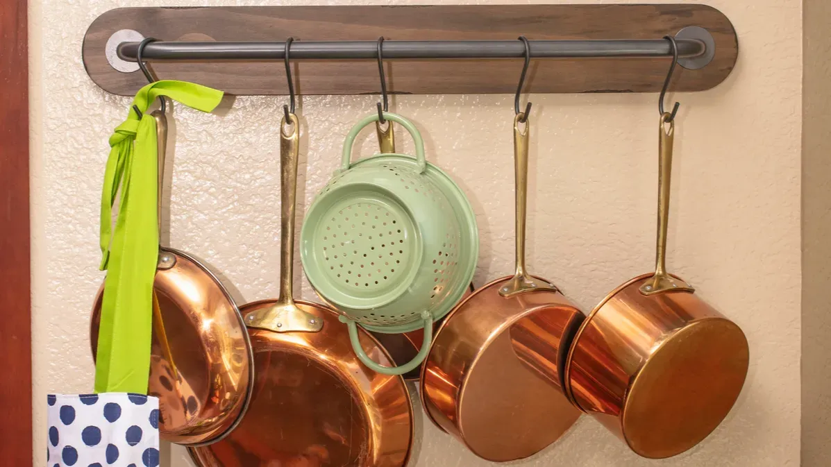 Pots and pans hanging on a tension rod using hooks.