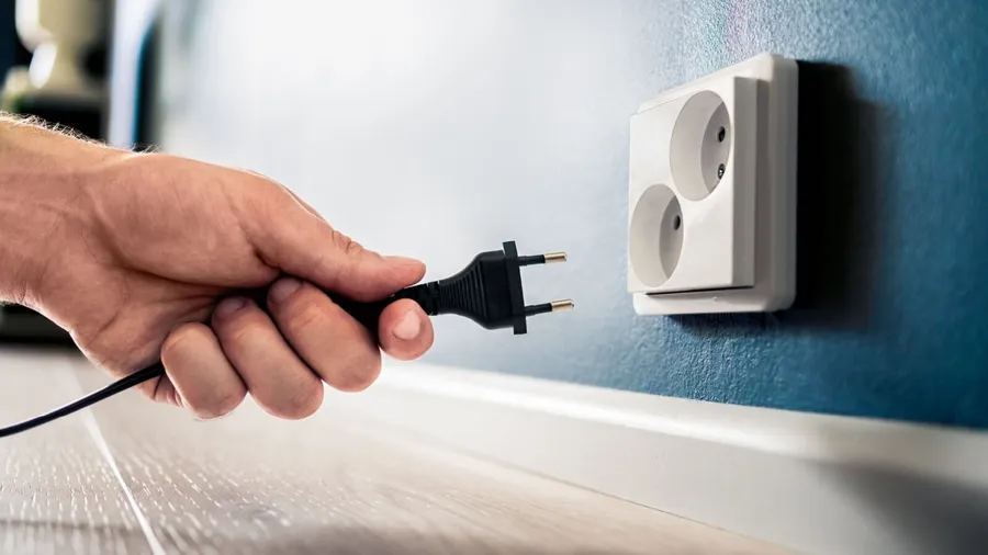 A person plugging a cord into a power outlet.