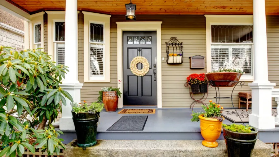 A porch with unique planters with vibrant blooming flowers in them, door mat, rug, and wreath on the door.