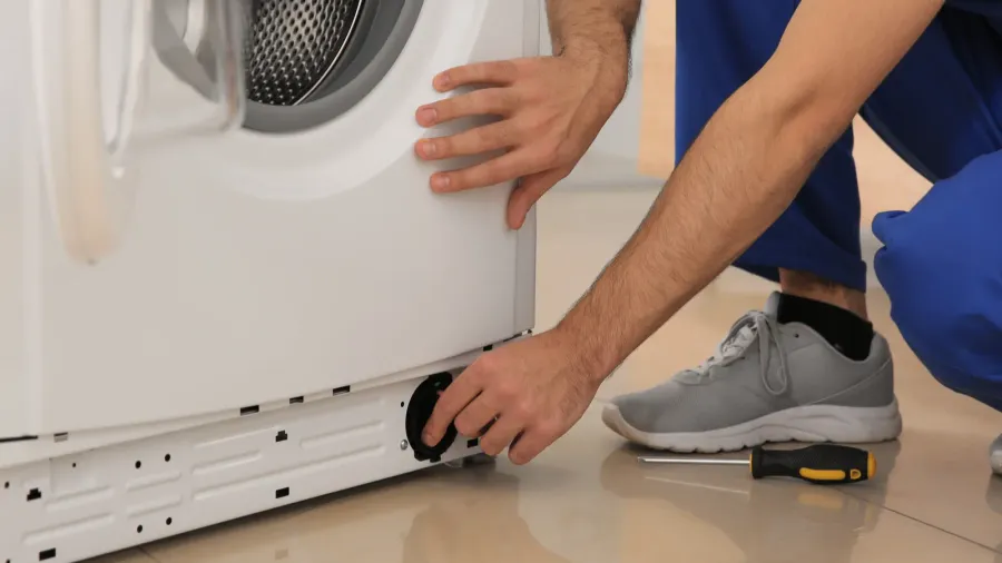 A person troubleshooting a washing machine, inspecting its underside.