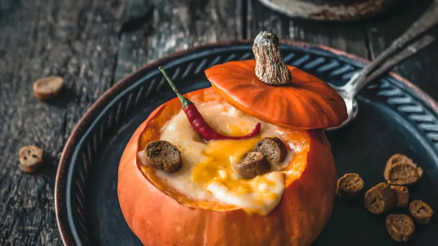 Pumpkin soup with chili pepper and cheese crust in baked pumpkins on plates on wooden table.