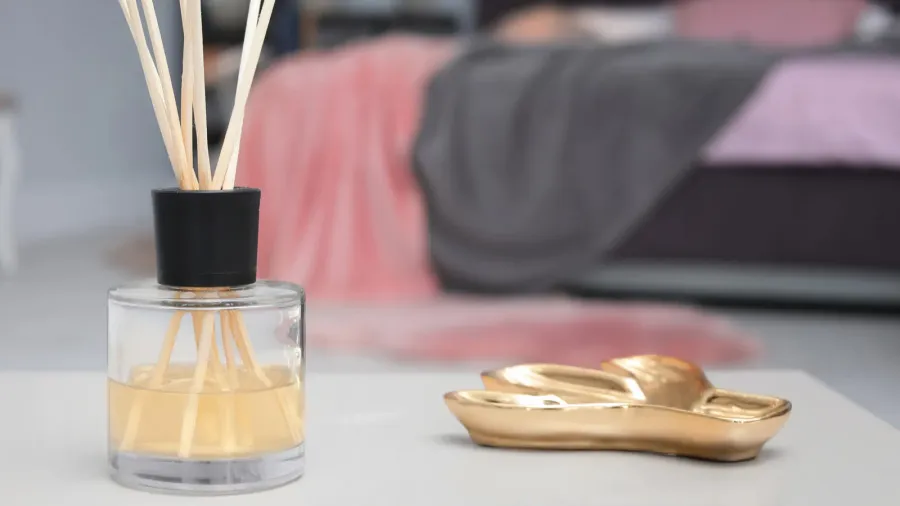 A reed diffuser and a small tray with metallic finish on a white table.