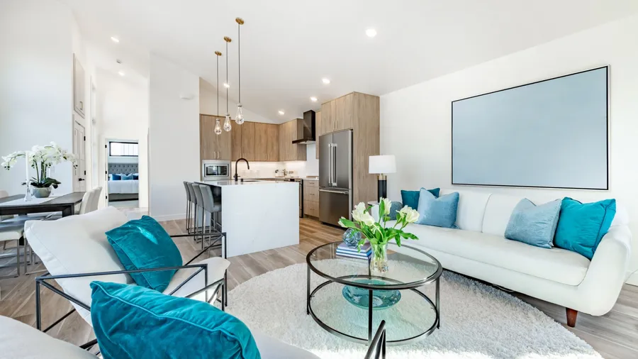 Home interior showing kitchen dining and living room decorated with blu White sofa round coffee table granite marble island with bar stools rectangle dining table with chair.