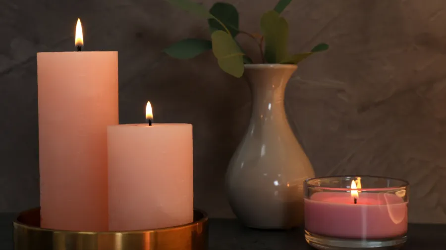 Two pink candles and a pink tealight candle with a small plant in a white vase in the background.