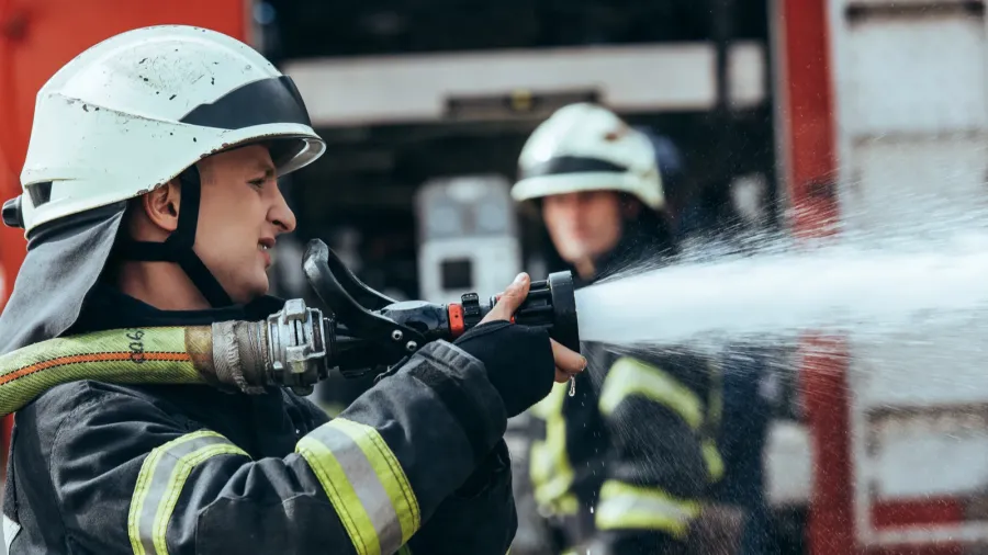 selective focus of firefighter with water hose extinguishing fire on
