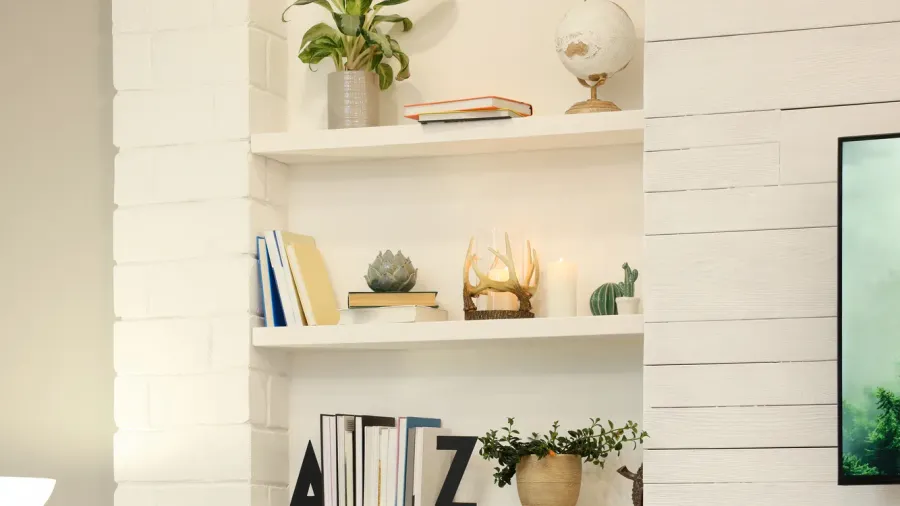 A white built-in shelf decorated with books, candles, potted plants, and decor accents including globe and ceramic paperweight.