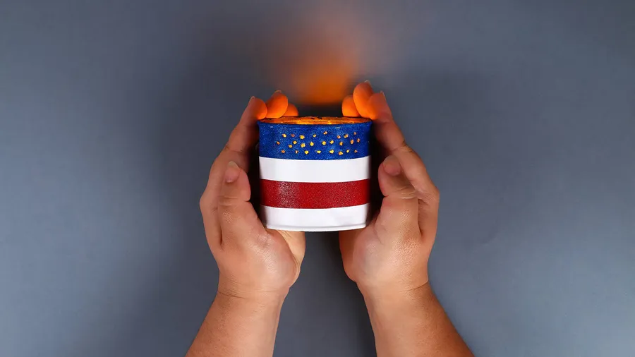 A person holding a DIY tin can luminary painted in blue, red, and white with a candle inside it.