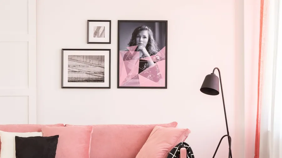 Gallery of pink-themed posters on empty white wall of bright living room interior with pastel pink settee.