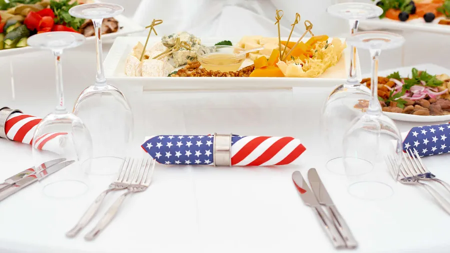 A table setting with utensils, glassware, USA flag napkins, and serving platters with food.