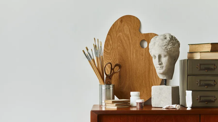 Stylish composition of artist workspace room with design retro teak commode, mock up poster frame, book, sculptural decoration and painting accessories.