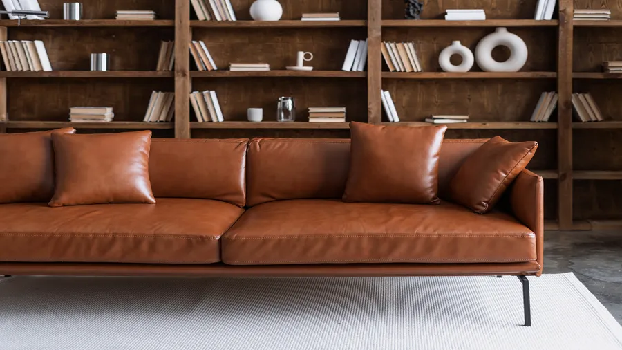 A home library with a leather sofa, wooden bookshelves, and a rug.