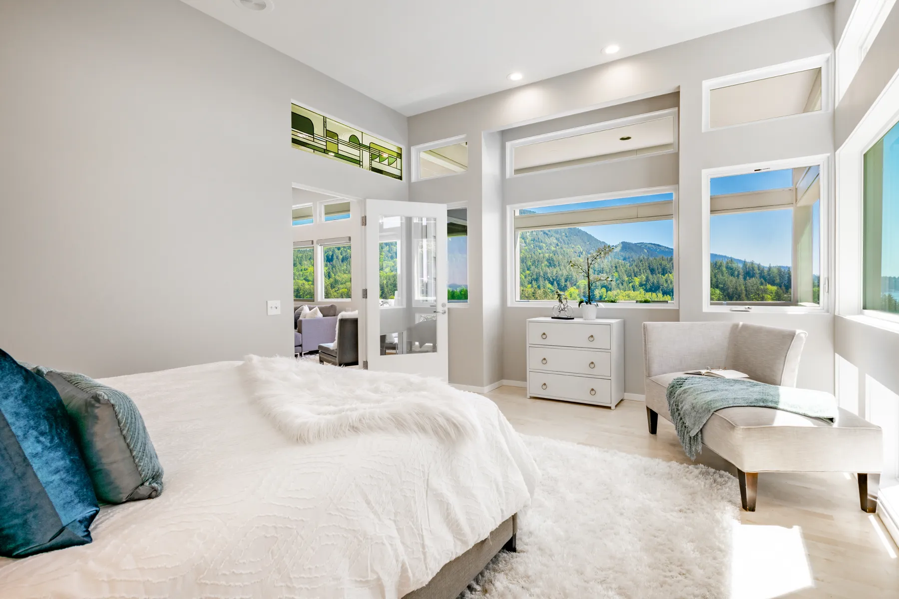 A bright, modern bedroom showcases a comfy bed with decorative pillows and large windows revealing a scenic view.