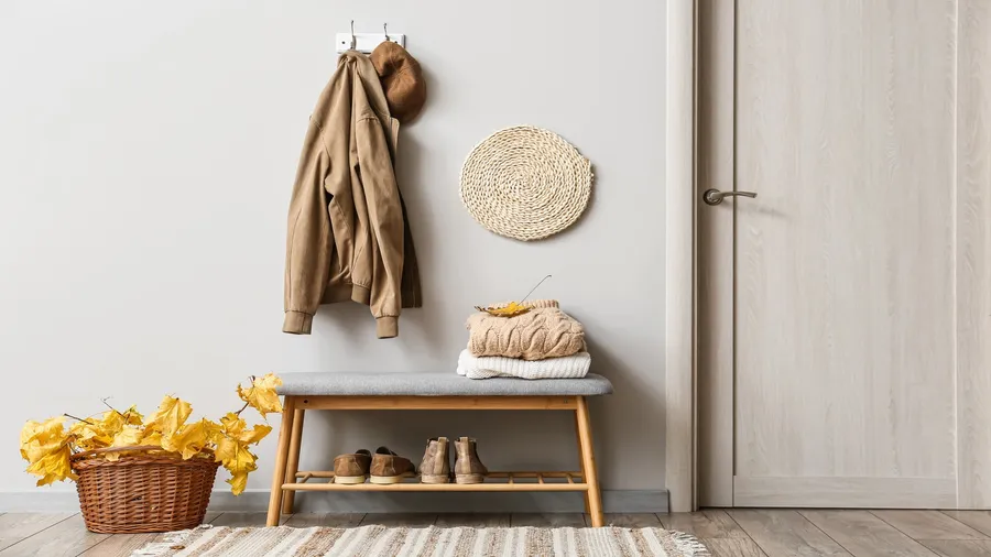 An entryway with a basket, bench with storage, rug, and hook attached on the wall with jackets.