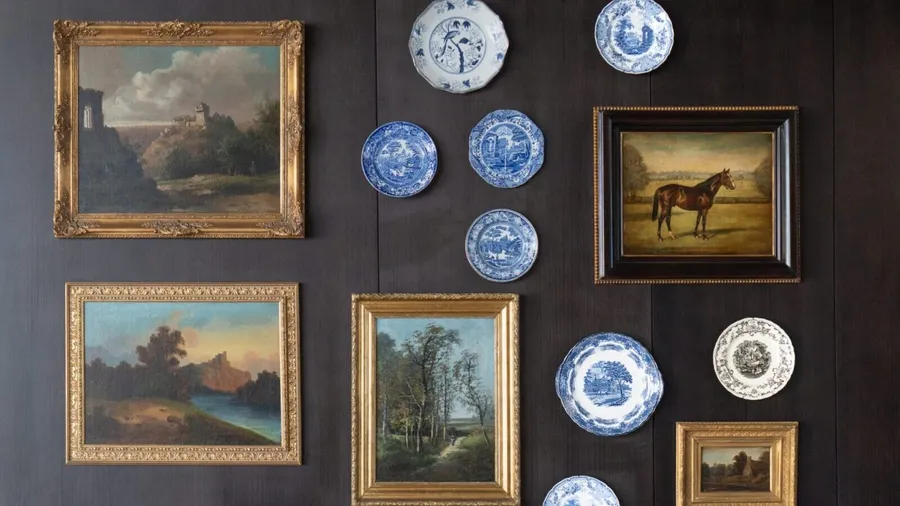 A gallery wall with a unique collection of paintings and decorative plates.
