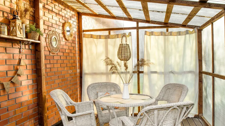 A beautiful patio with rattan table and chairs, decor accents on brick wall, and curtains around the pergola.
