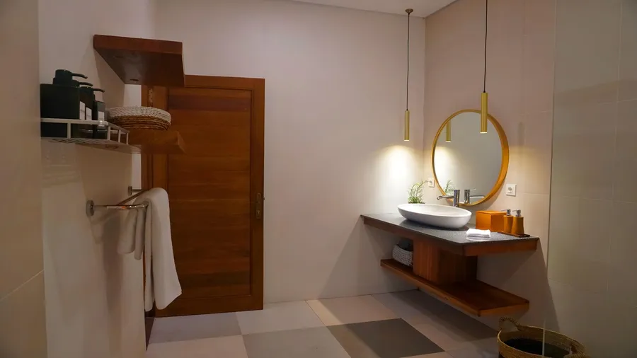 A modern bathroom featuring a floating wooden vanity with a vessel sink, a round mirror, pendant lighting, and wooden floating shelves.