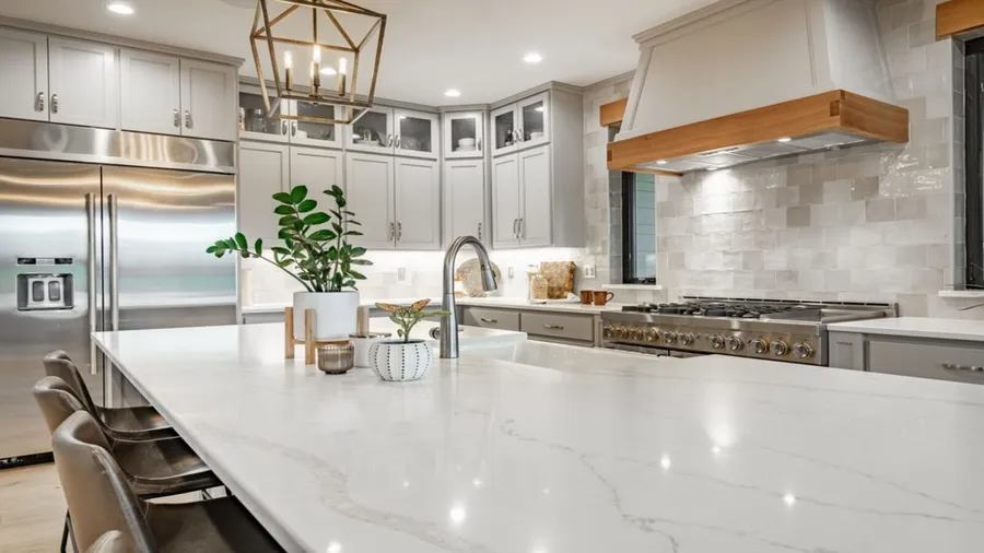 A kitchen interior with white cabinets, small potted plant, fridge, and quartz countertop.