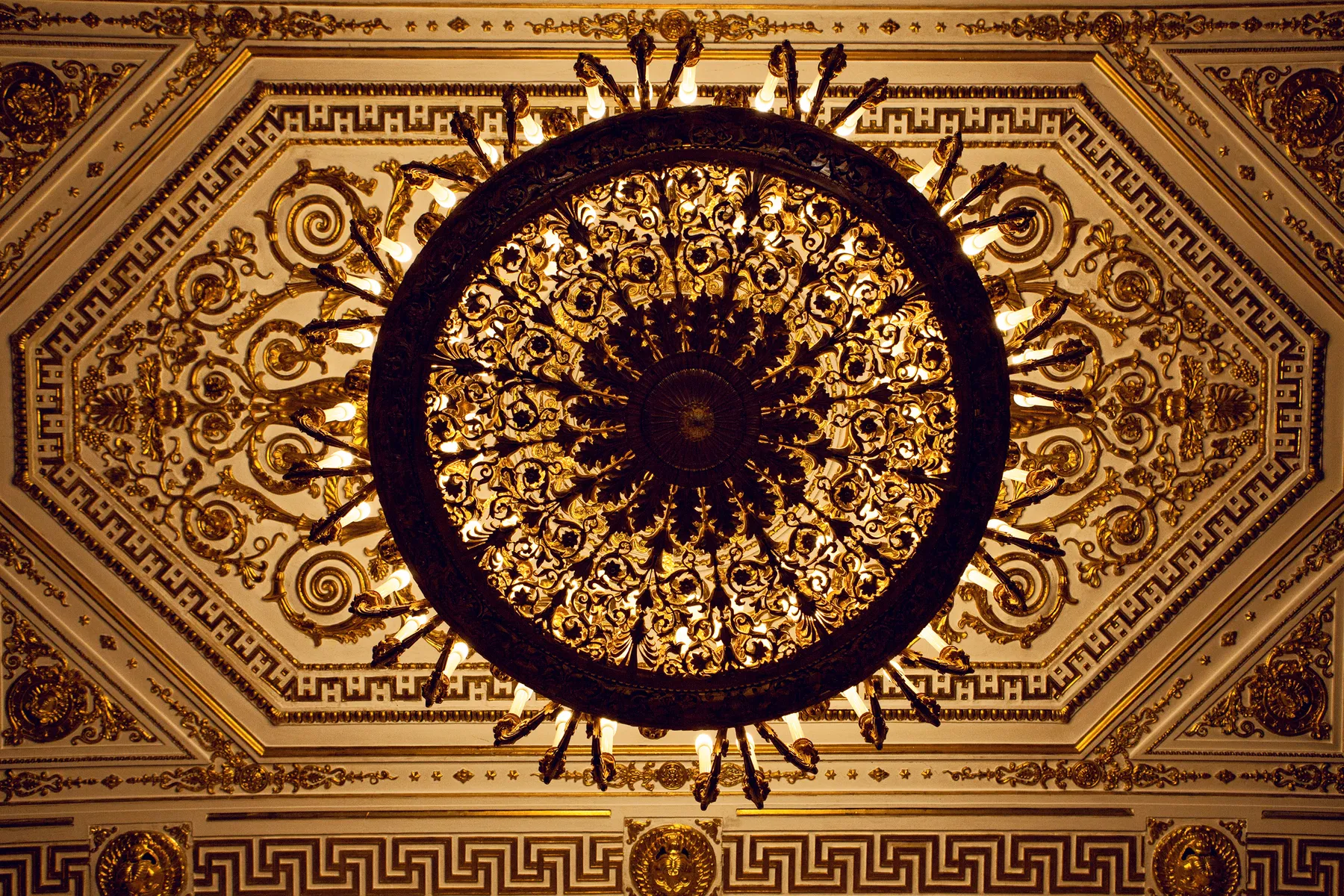 Elegant chandelier with intricate gold details on a ceiling.