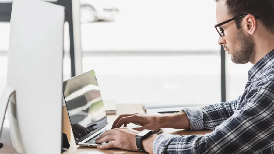side view of handsome young programmer in eyeglasses working with
