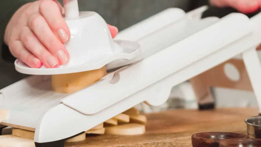 A person slicing potatoes with mandoline slicer on a wooden surface.