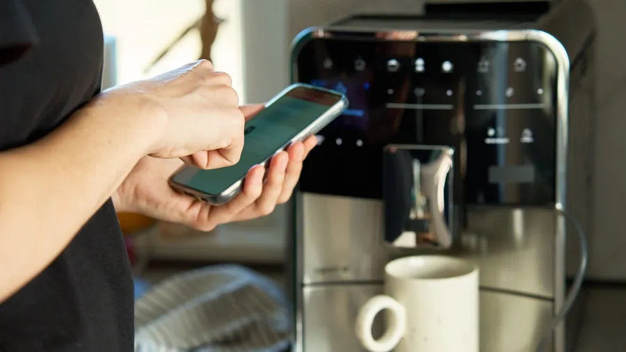 A woman operating a coffee machine with her smartphone.