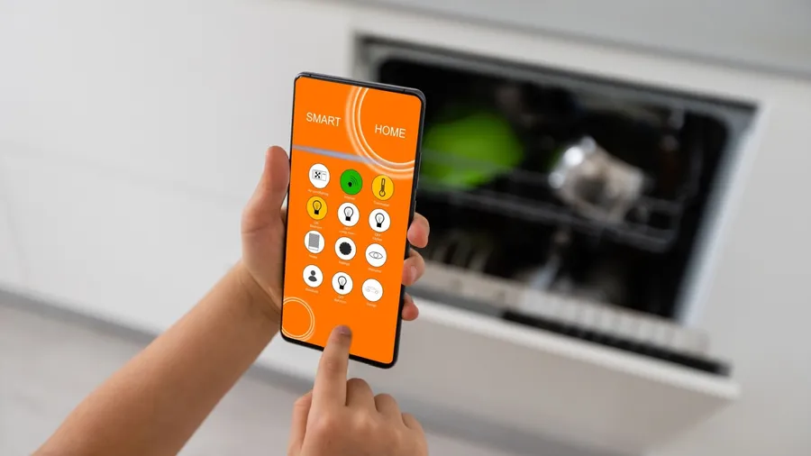 A person using a smartphone to operate a smart dishwasher.