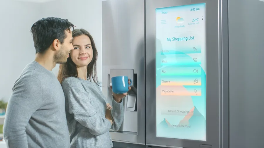A couple standing in front of a smart refrigerator displaying grocery list.